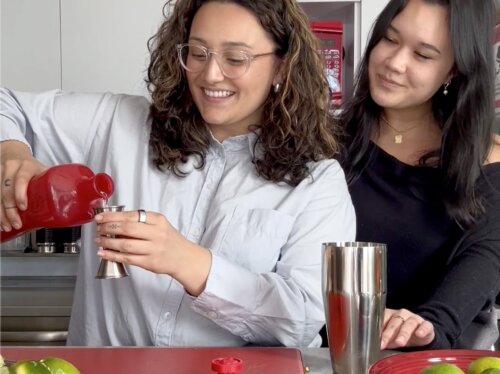 Woman pours (LOBOS 1707)ᴿᴱᴰ tequila into cocktail jigger while other woman looks over her shoulder