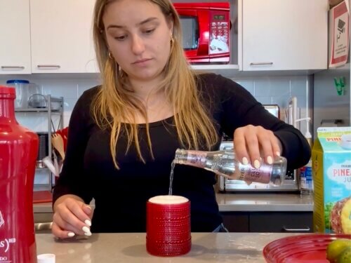Woman pours club soda into decorative cocktail glass