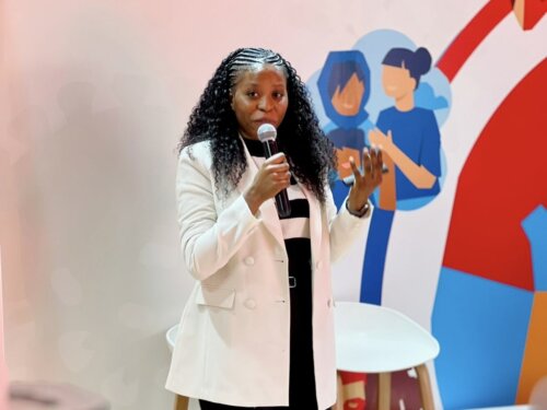 Cynthia Kasonde, a medical technologist & QMS Specialist at CHAZ Laboratory, and a Health advocate for the (RED) and Roche partnership, wears her labcoat and holds a microphone at IAS.